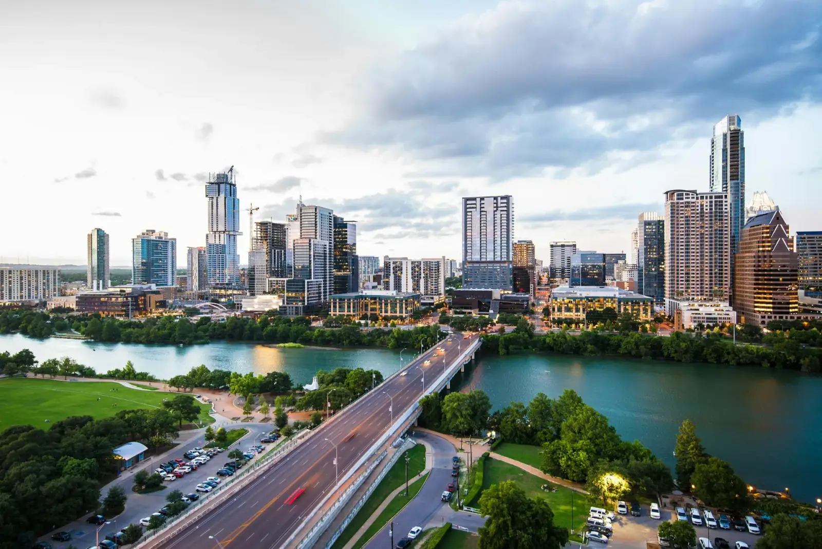 Austin Texas skyline with tall buildings, a river, a bridge, and green park areas at dusk.