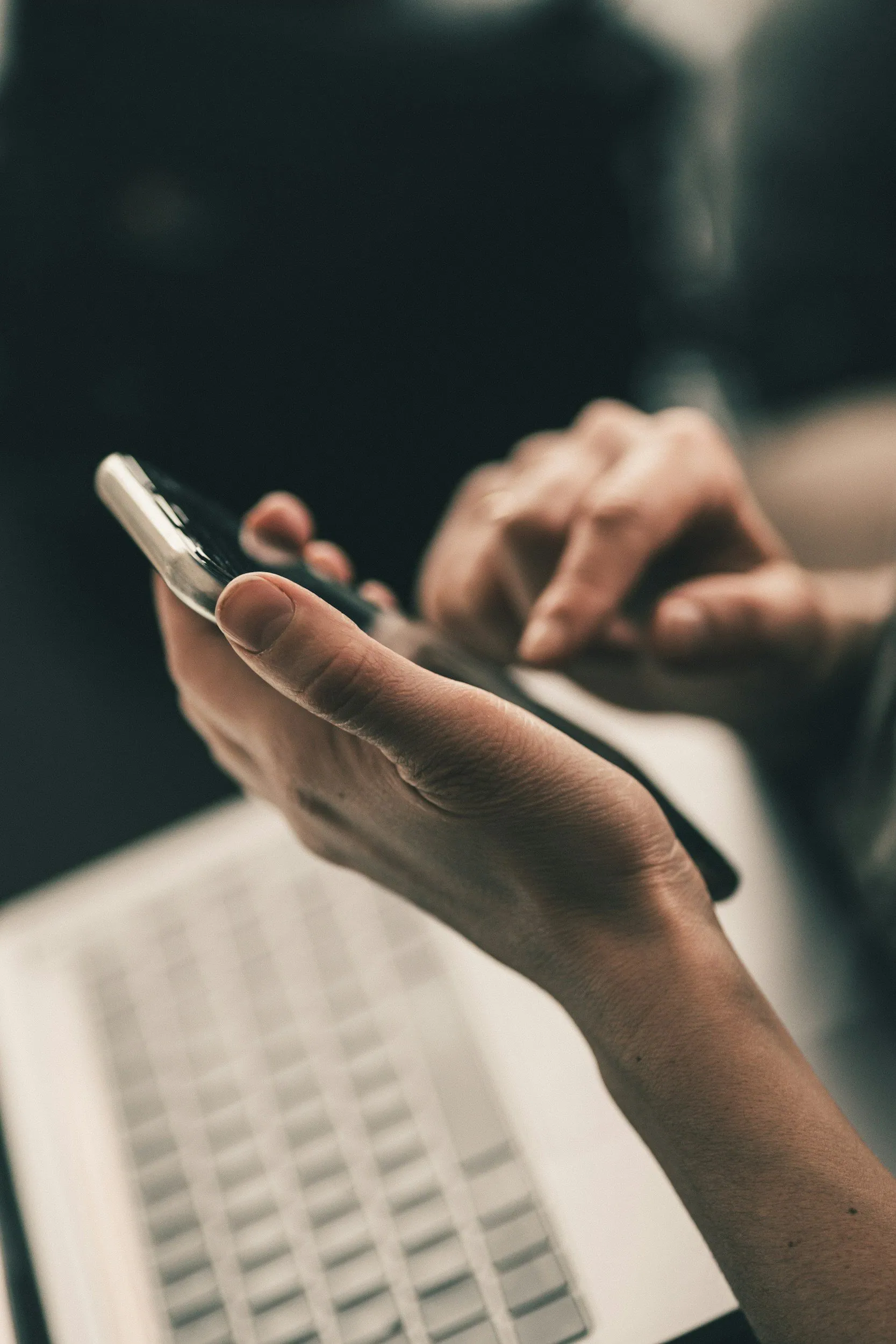 Close-up of hands holding and using a smartphone, with a keyboard partially visible beneath the hands.