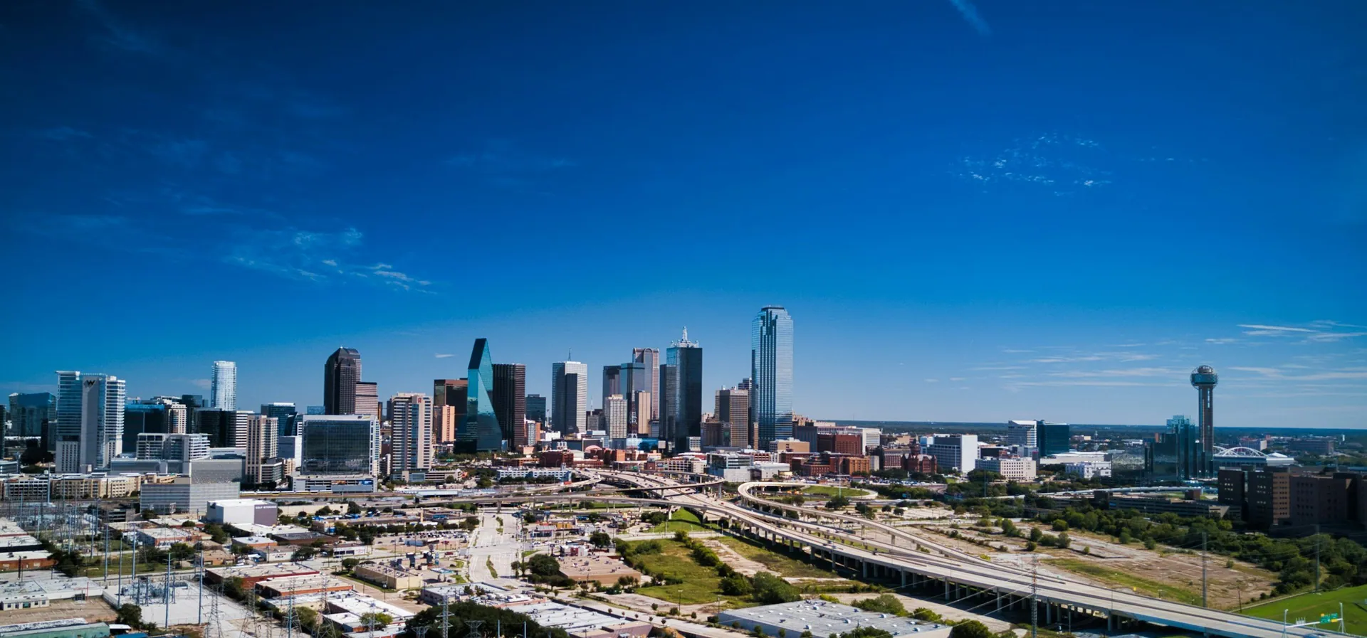A city skyline featuring tall skyscrapers, highways, and a clear blue sky.